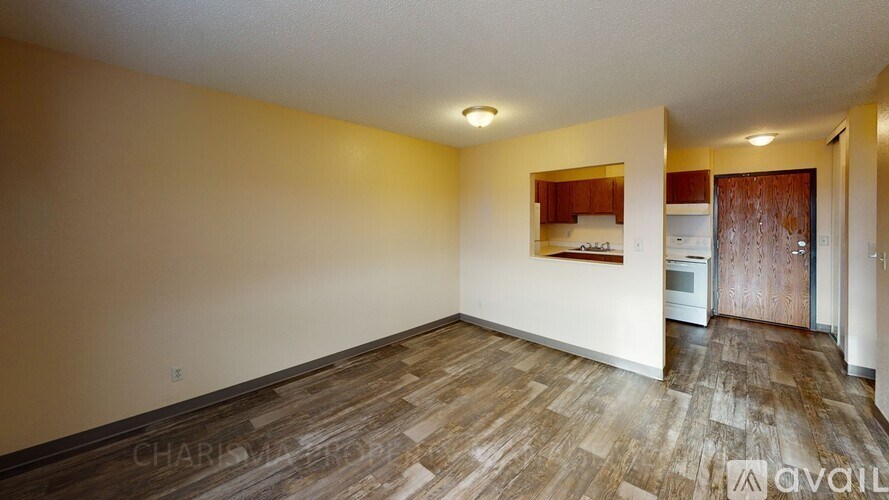 A room with wooden flooring and a kitchen area in the background.