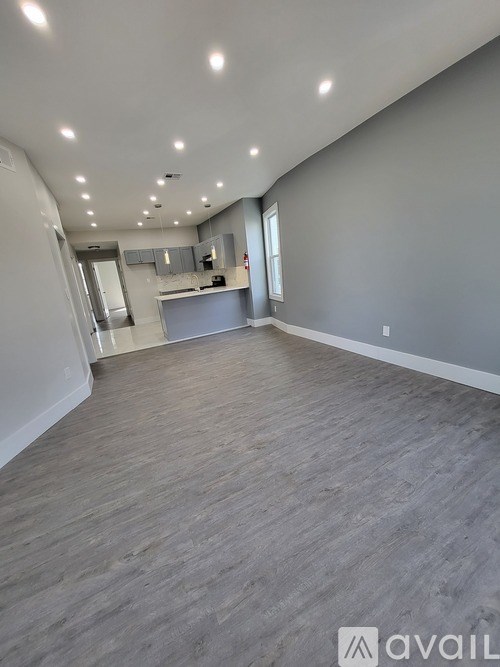A spacious room with grey flooring and a kitchen area in the background.