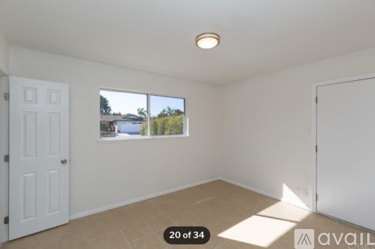 A room with a window showing a view of a house and trees outside.
