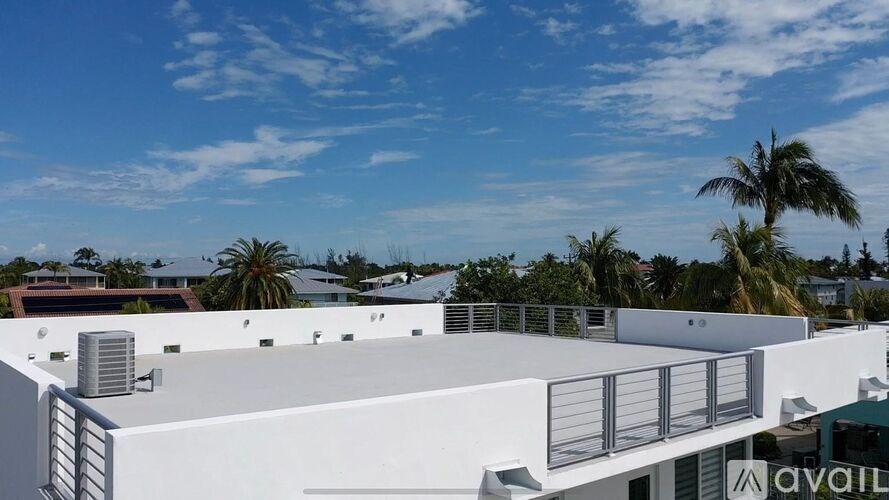 A white building with a balcony and palm trees in the background.