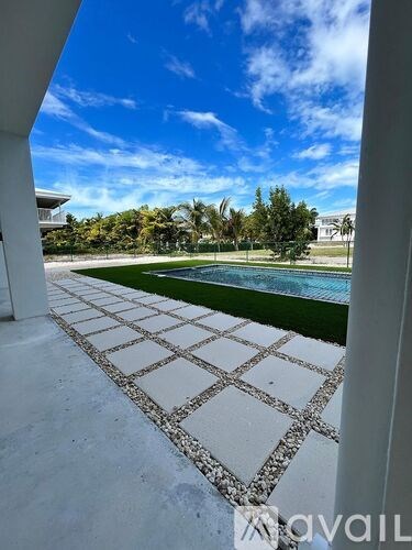 A tiled walkway leads to a pool area with a clear blue sky above.