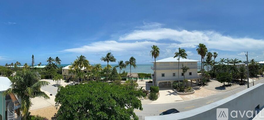 A white building with a balcony is surrounded by palm trees.