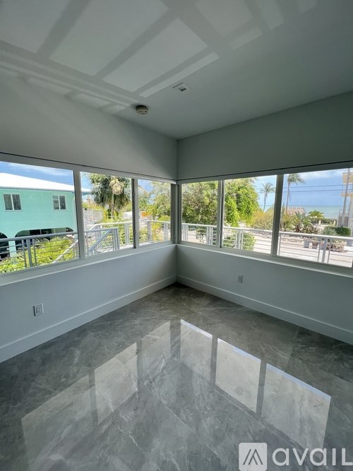 A room with a marble floor and large windows overlooking a green building.
