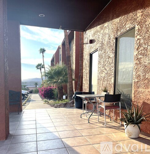 A patio with a table and chairs overlooks a street with palm trees.