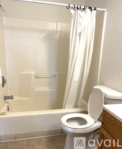 A white toilet is in a bathroom with a white shower curtain.