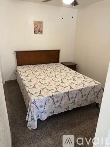 A bed with a patterned cover sits in a room with a ceiling fan.