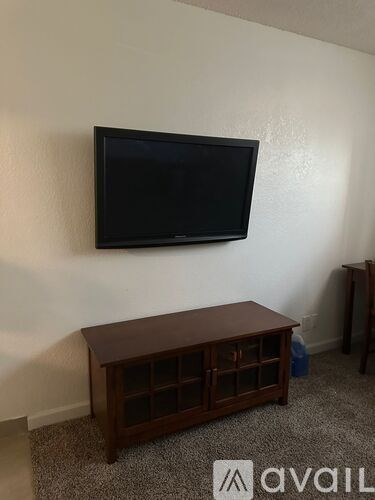 A black television is mounted on a white wall above a wooden cabinet.