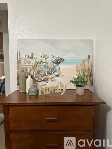 A painting of a beach scene with a bicycle is displayed on a wooden dresser.