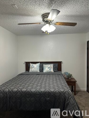A bedroom with a bed, a ceiling fan, and a nightstand.