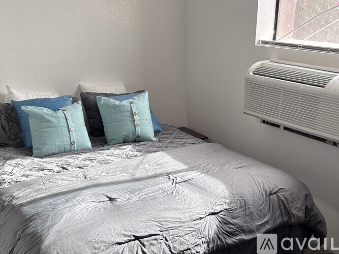 A bed with a white comforter and four blue pillows with silver buckles.
