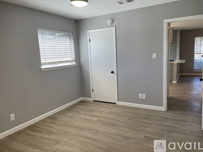 A room with a white door, a window with blinds, and a wooden floor.