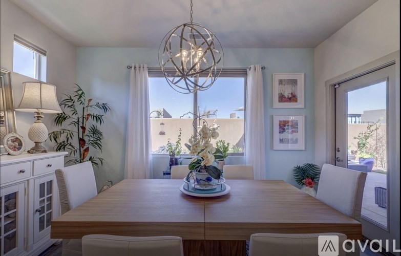 A dining room with a wooden table and chairs, a chandelier, and a view of the outside through the windows.