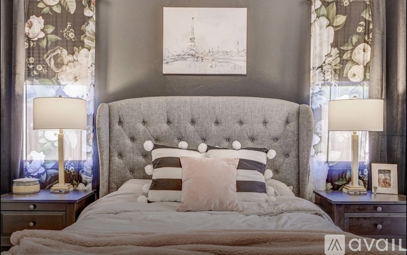 A bedroom with a large bed, two lamps, and a painting on the wall.