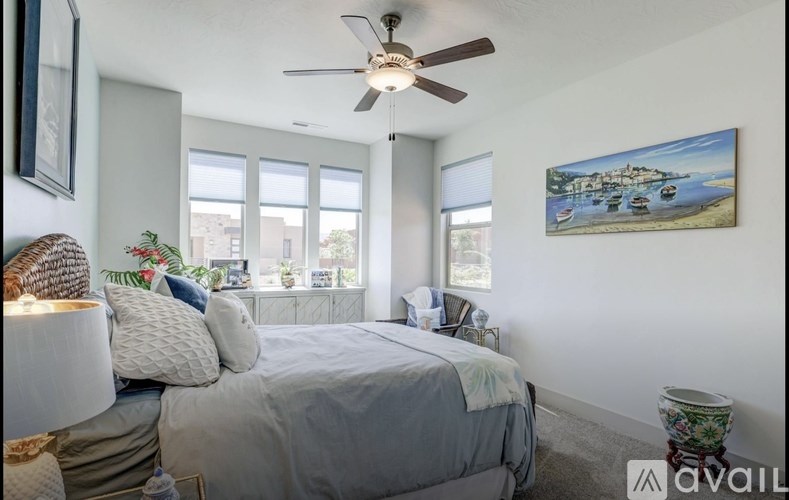 A bedroom with a bed, a ceiling fan, and a painting on the wall.