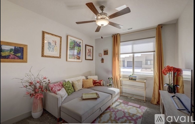 A living room with a grey couch, a fan, and a painting on the wall.