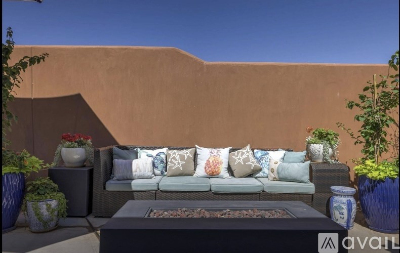 A patio with a couch, pillows, and potted plants.