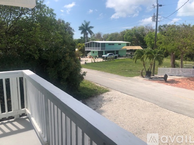 A balcony overlooks a green yard and a road.