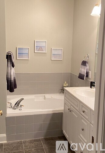 A bathroom with a white bathtub and grey tiles.
