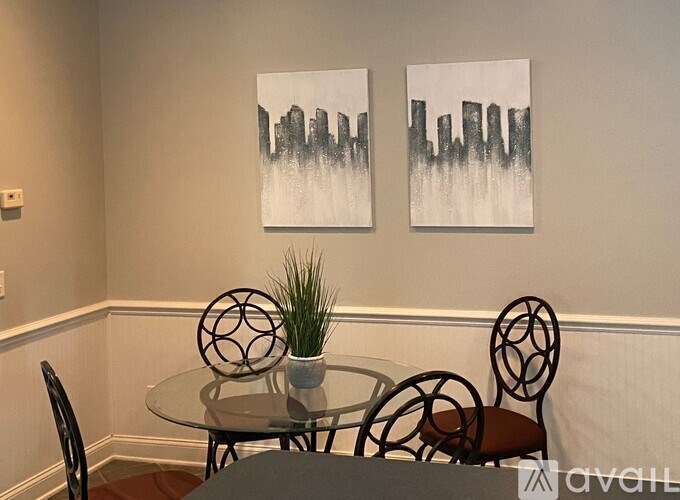 A dining room with a glass table and chairs and two paintings on the wall.