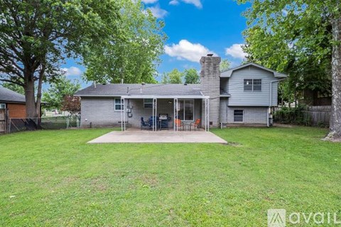 A house with a grey roof and a white chimney is surrounded by a green lawn and trees.