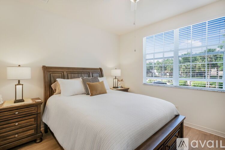 A bedroom with a large bed, a nightstand with a lamp, and a window with blinds.