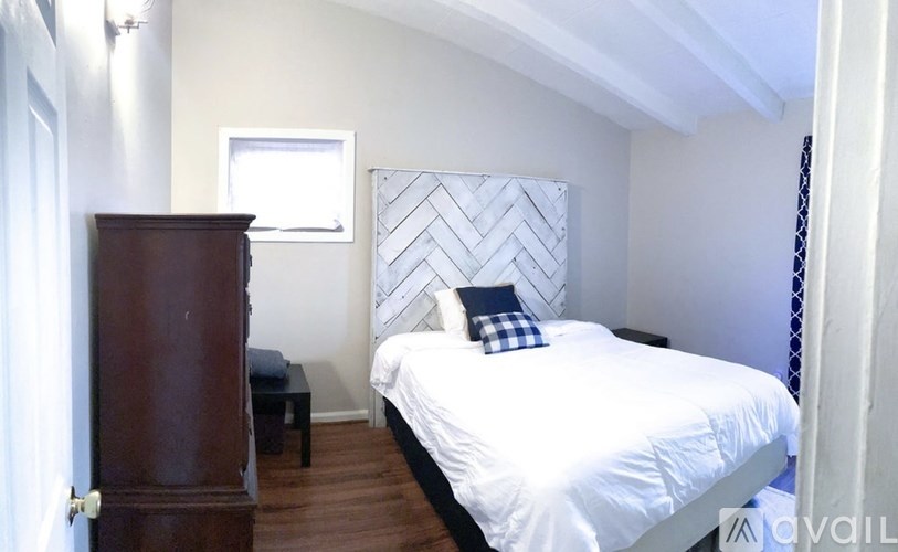 A bedroom with a white bed and a wooden dresser.