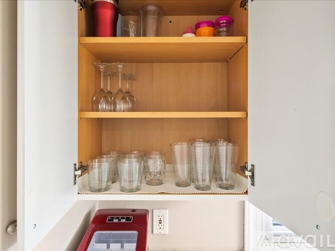 A kitchen cabinet with glasses and cups on the shelf.