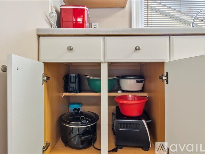 A kitchen cabinet with a black pot on the bottom shelf and a red bowl on top.