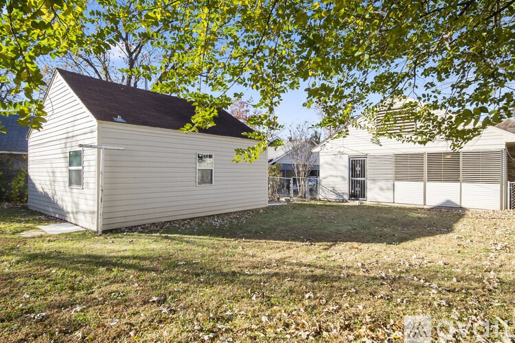 A small white house with a brown roof is surrounded by trees with yellow leaves.