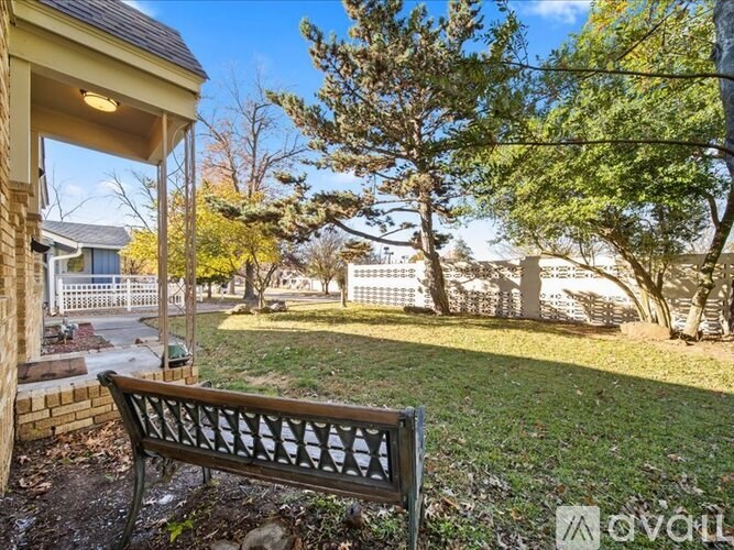 A bench is situated in a yard with a house and trees in the background.