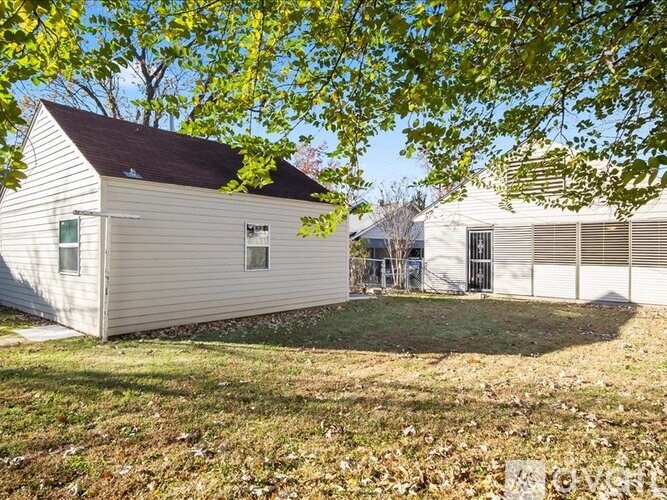 A small white house with a brown roof is surrounded by trees.