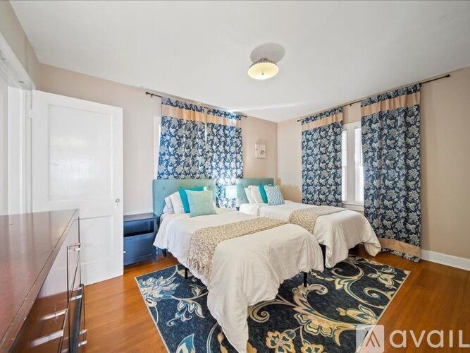 A bedroom with two beds and a rug in the center.