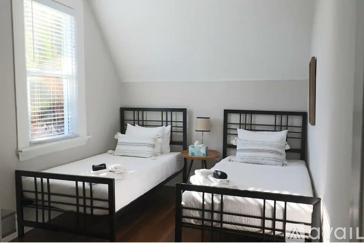 Two beds with white bedspreads and pillows in a room with white walls.