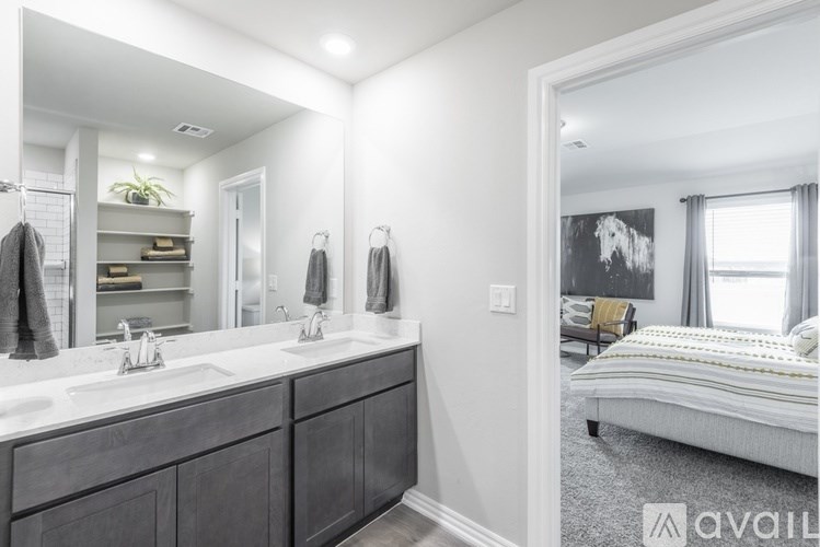 A bathroom with a double sink vanity and a bedroom with a bed and a window.