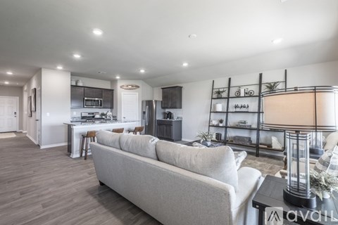 A modern living room with a grey sofa and a kitchen area in the background.