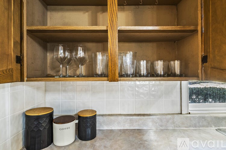 A kitchen with a wooden cabinet and glasses on the shelf.