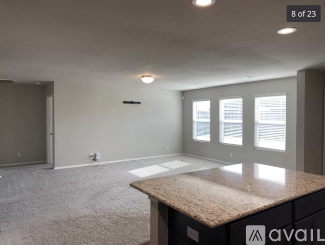 A spacious room with a carpeted floor, a granite countertop, and a window with blinds.