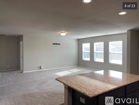 A spacious room with a carpeted floor, a granite countertop, and a window with blinds.