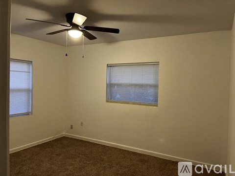 A room with a ceiling fan and two windows.
