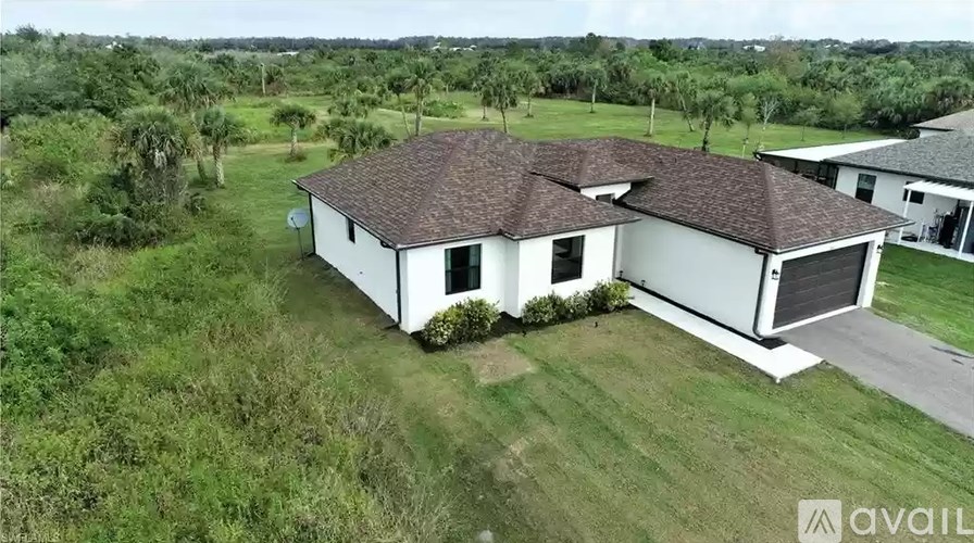 A white house with a brown roof is surrounded by greenery.