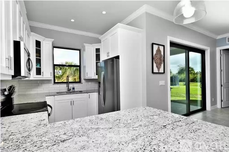 A modern kitchen with a marble floor and a view of the backyard through the glass doors.