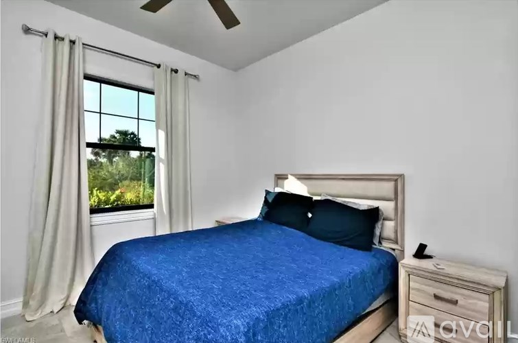 A bedroom with a blue bedspread and a window with curtains.