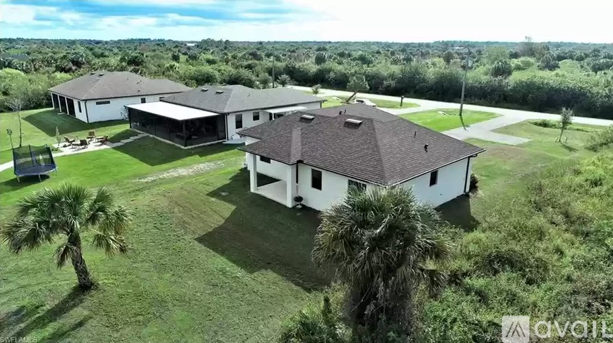 A large white house with a brown roof is surrounded by greenery and palm trees.