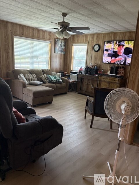 A living room with a television, a couch, a chair, and a fan.