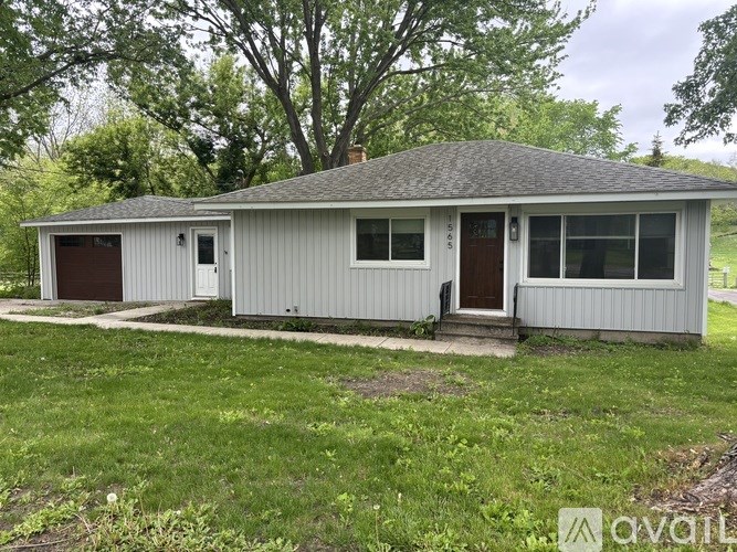 A two-story house with a garage is surrounded by green grass and trees.