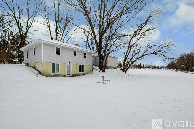 A house in a snowy field with bare trees.