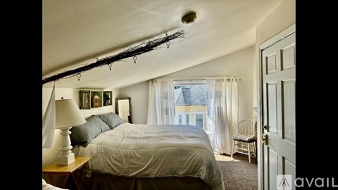 A bedroom with a bed, chair, and a window with curtains.