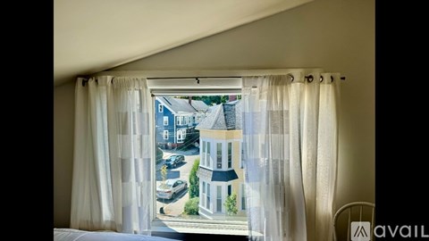 A window with curtains showing a street view with cars and buildings.