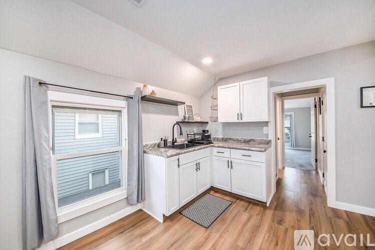 A kitchen with white cabinets and a window with grey curtains.