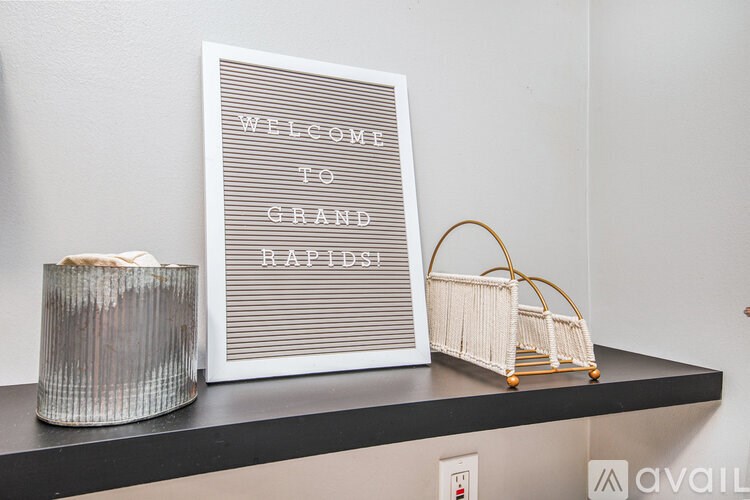 A framed sign that says "Welcome to Grand Rapids" is on a shelf next to a candle and a basket.